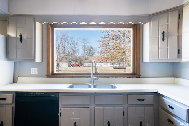 kitchen with black dishwasher, light countertops, a sink, and gray cabinetry