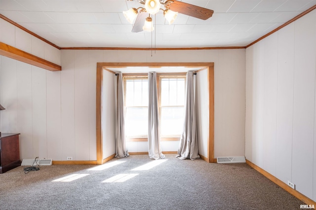 carpeted empty room with ceiling fan, ornamental molding, visible vents, and baseboards