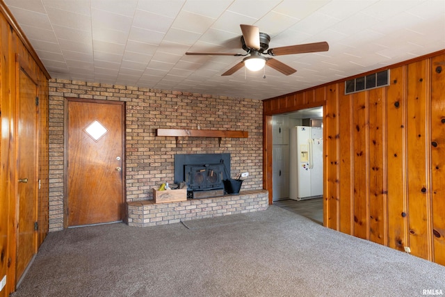 unfurnished living room with carpet floors, a wood stove, visible vents, and wood walls