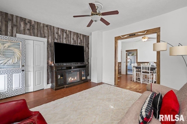 living room with ceiling fan, a glass covered fireplace, wood walls, and wood finished floors