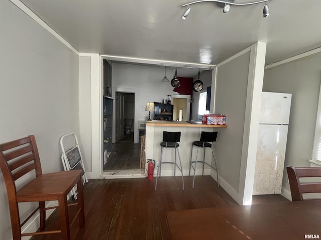 kitchen featuring a peninsula, dark wood-style flooring, baseboards, freestanding refrigerator, and a kitchen bar