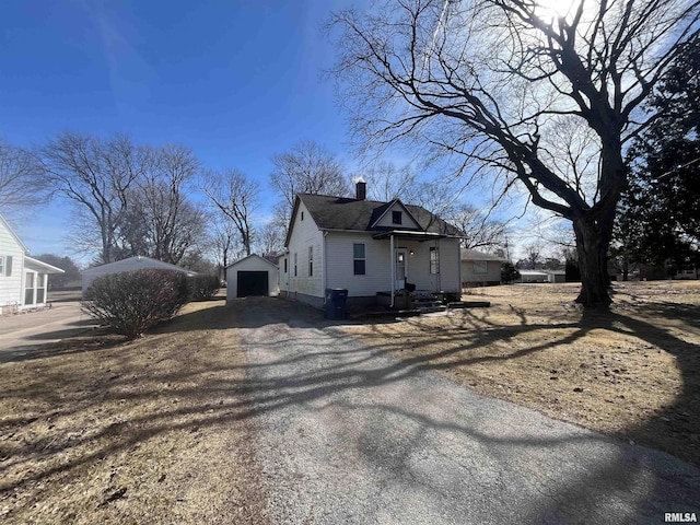 view of property exterior with a garage, an outdoor structure, driveway, roof with shingles, and a chimney