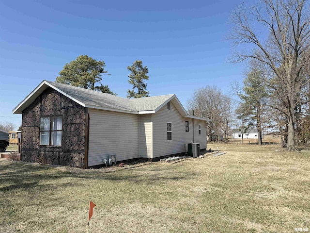 view of home's exterior featuring stone siding, central AC unit, and a yard