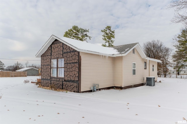 view of snow covered exterior with stone siding and central AC unit