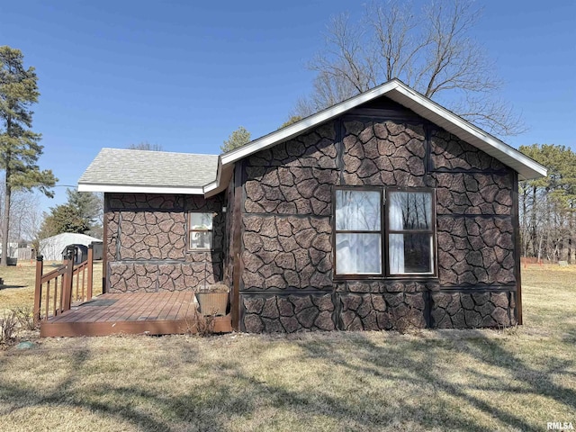 view of side of home featuring stone siding, a yard, roof with shingles, and a wooden deck