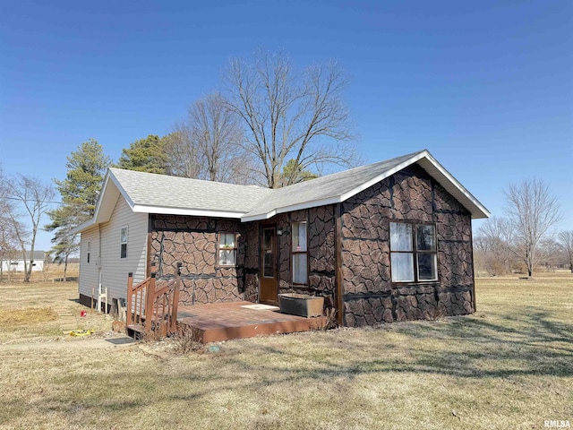 view of property exterior featuring stone siding, a lawn, and roof with shingles