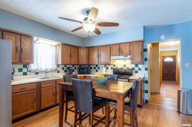 kitchen with brown cabinetry, stainless steel range with electric cooktop, a sink, black microwave, and under cabinet range hood