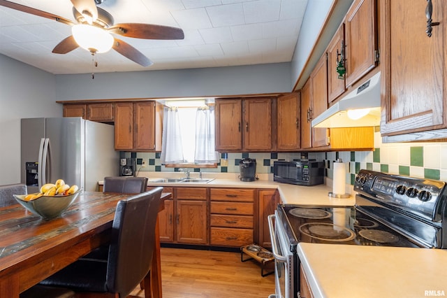 kitchen with under cabinet range hood, a sink, light countertops, black appliances, and brown cabinetry