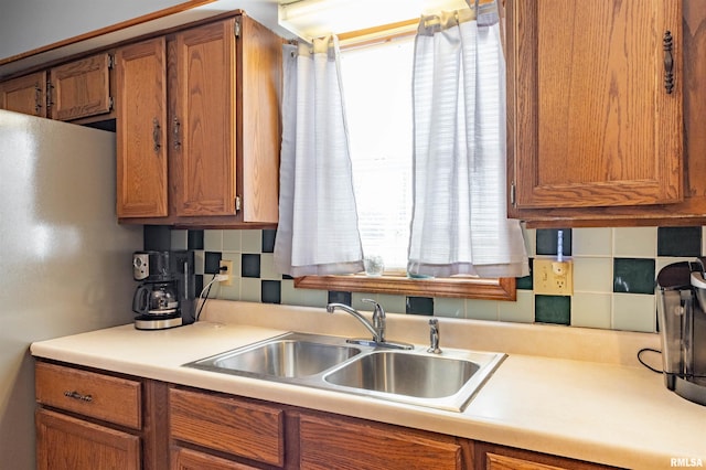 kitchen featuring light countertops, tasteful backsplash, a sink, and brown cabinets