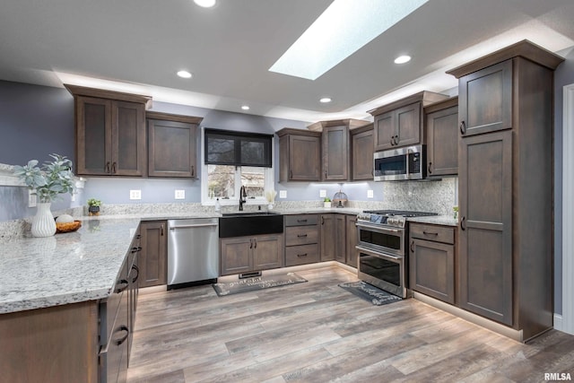 kitchen featuring a skylight, light wood-style flooring, appliances with stainless steel finishes, and a sink