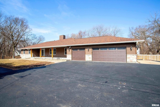 single story home featuring driveway, a garage, stone siding, a chimney, and fence