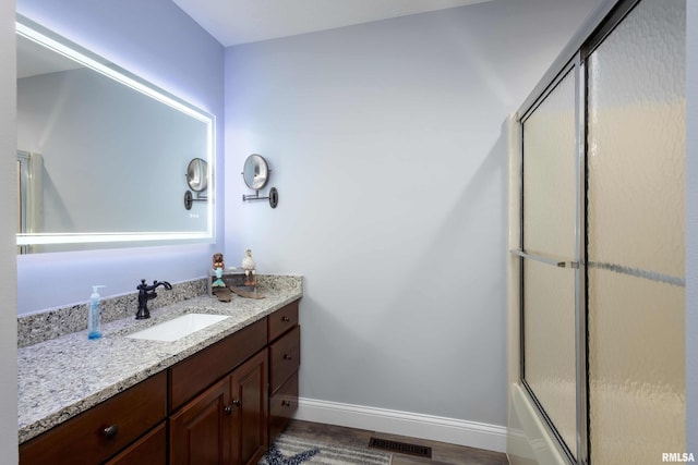 bathroom with a shower with door, visible vents, vanity, wood finished floors, and baseboards