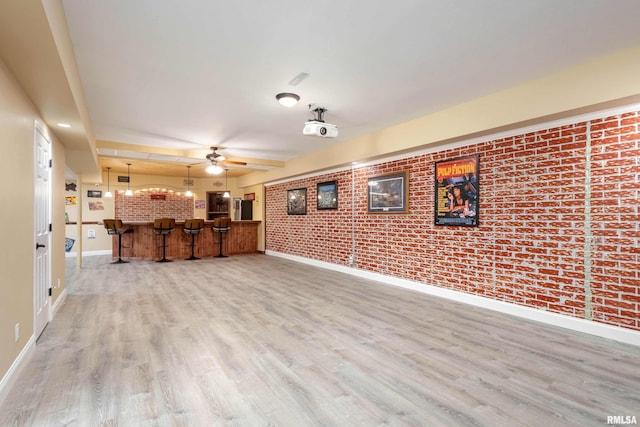 unfurnished living room with bar, brick wall, wood finished floors, a ceiling fan, and baseboards