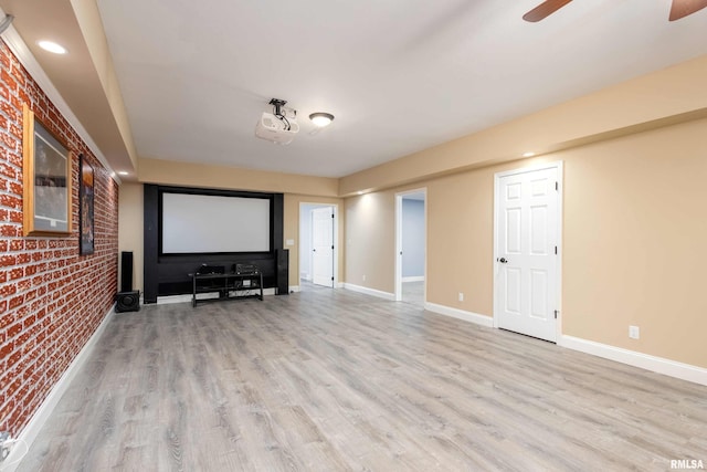 home theater room with a ceiling fan, brick wall, baseboards, and light wood finished floors