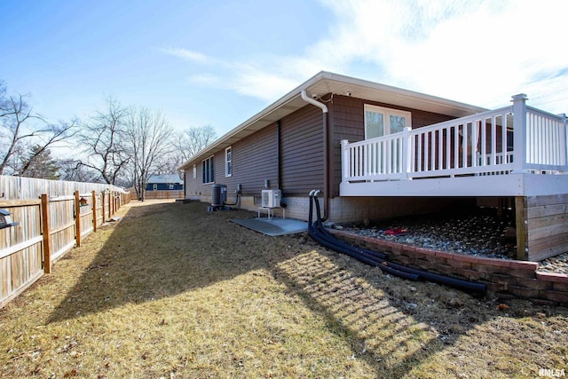 view of side of home featuring a deck, a fenced backyard, a yard, and central AC