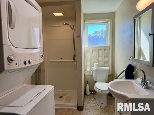 bathroom with toilet, a stall shower, a sink, and stacked washer / drying machine