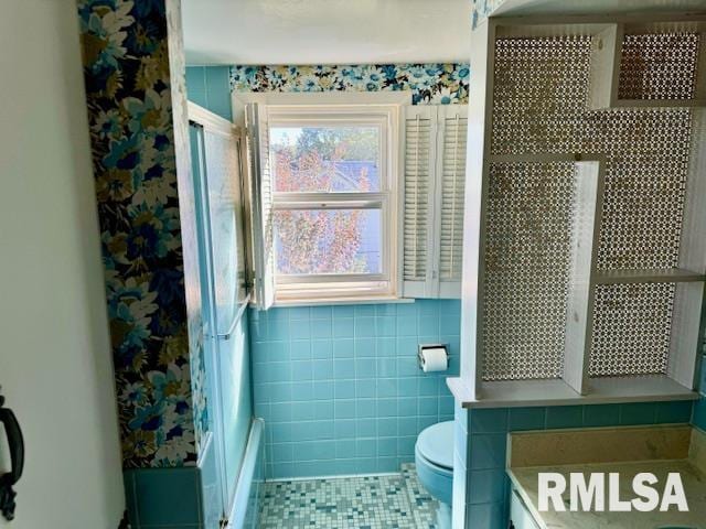 bathroom featuring tile patterned flooring, a shower with shower door, tile walls, and toilet