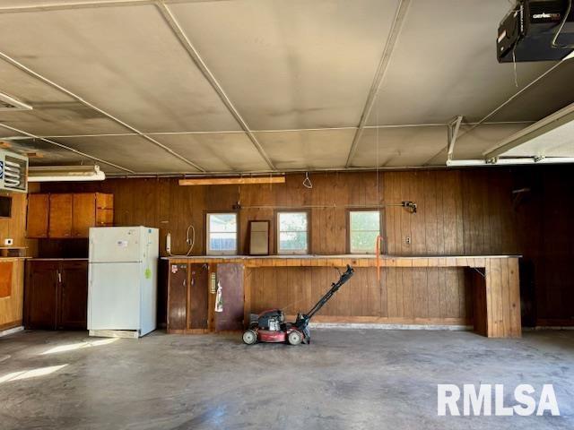 garage with wood walls, freestanding refrigerator, and a garage door opener