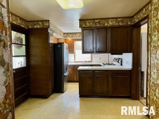 kitchen with white range oven, freestanding refrigerator, light countertops, dark brown cabinets, and light floors