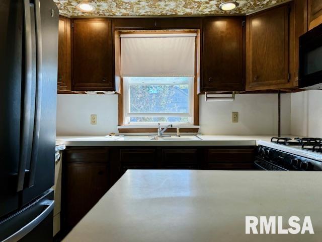 kitchen with white gas range, light countertops, freestanding refrigerator, a sink, and black microwave