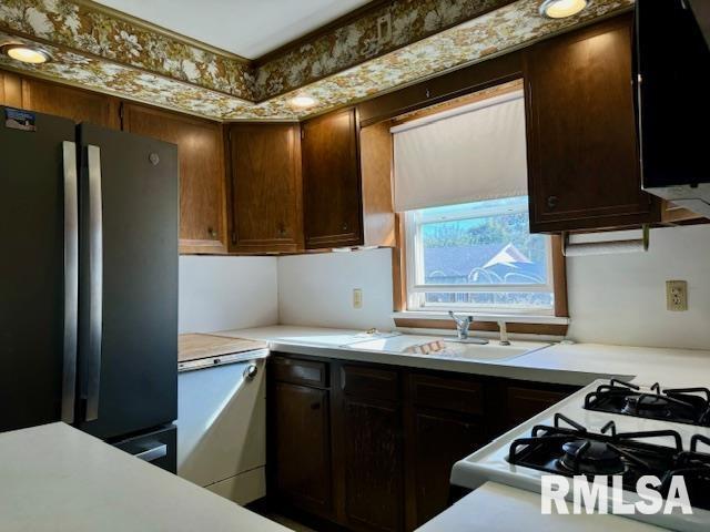 kitchen featuring light countertops, freestanding refrigerator, dark brown cabinetry, a sink, and gas range