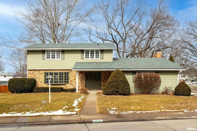 traditional-style house with roof with shingles, a chimney, a front yard, brick siding, and fence