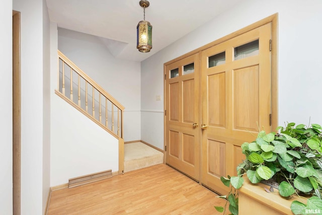 foyer with stairway, light wood-style flooring, visible vents, and baseboards