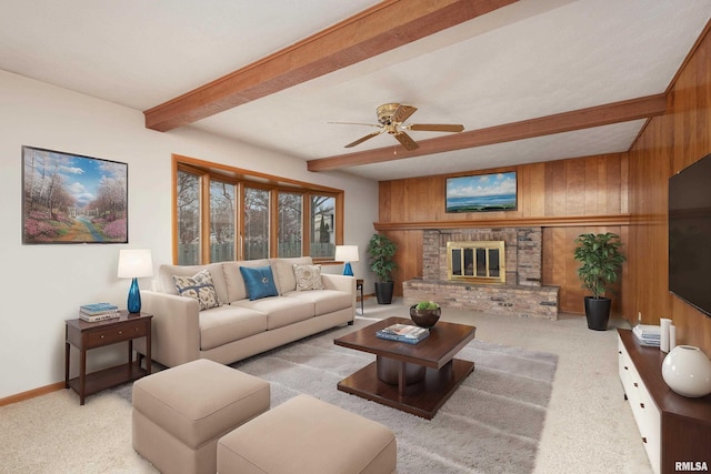 carpeted living area featuring beam ceiling, a ceiling fan, a brick fireplace, wooden walls, and baseboards