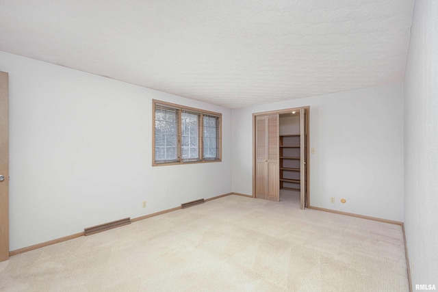 spare room featuring light carpet, baseboards, visible vents, and a textured ceiling