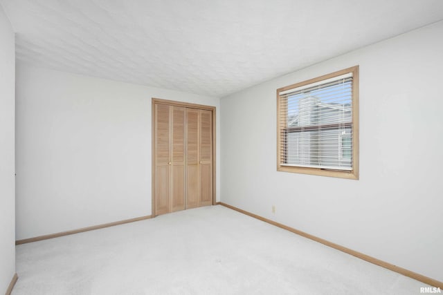 unfurnished bedroom with light carpet, a textured ceiling, baseboards, and a closet