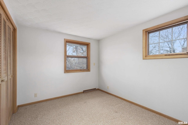 unfurnished bedroom with light carpet, a closet, visible vents, and baseboards