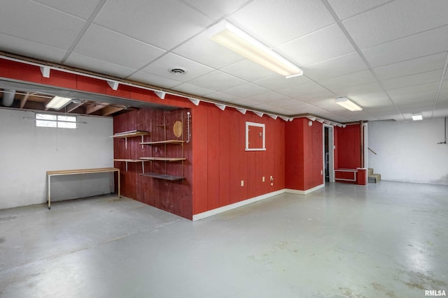 basement with a paneled ceiling, electric panel, and wooden walls