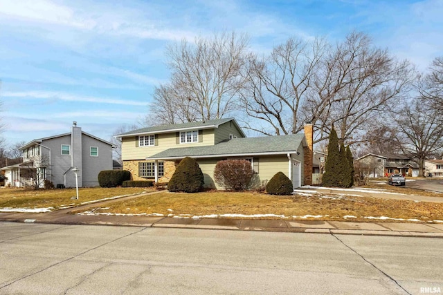 traditional-style home featuring a garage, driveway, a shingled roof, a chimney, and a front yard