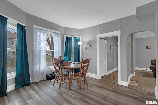 dining area with arched walkways, a textured ceiling, wood finished floors, and baseboards