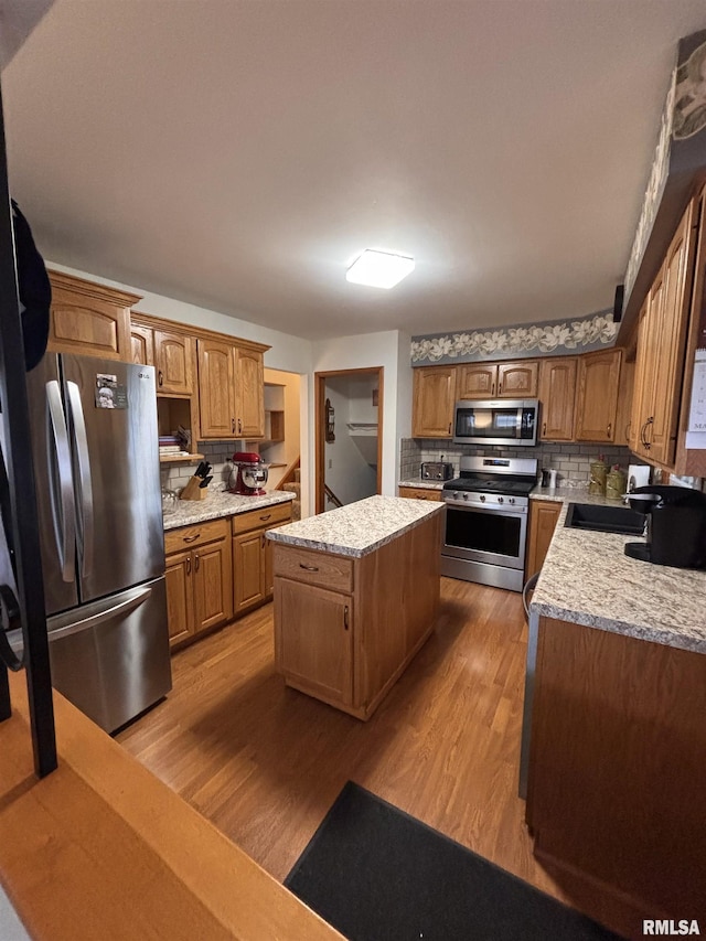 kitchen featuring a center island, tasteful backsplash, appliances with stainless steel finishes, a sink, and light wood-type flooring