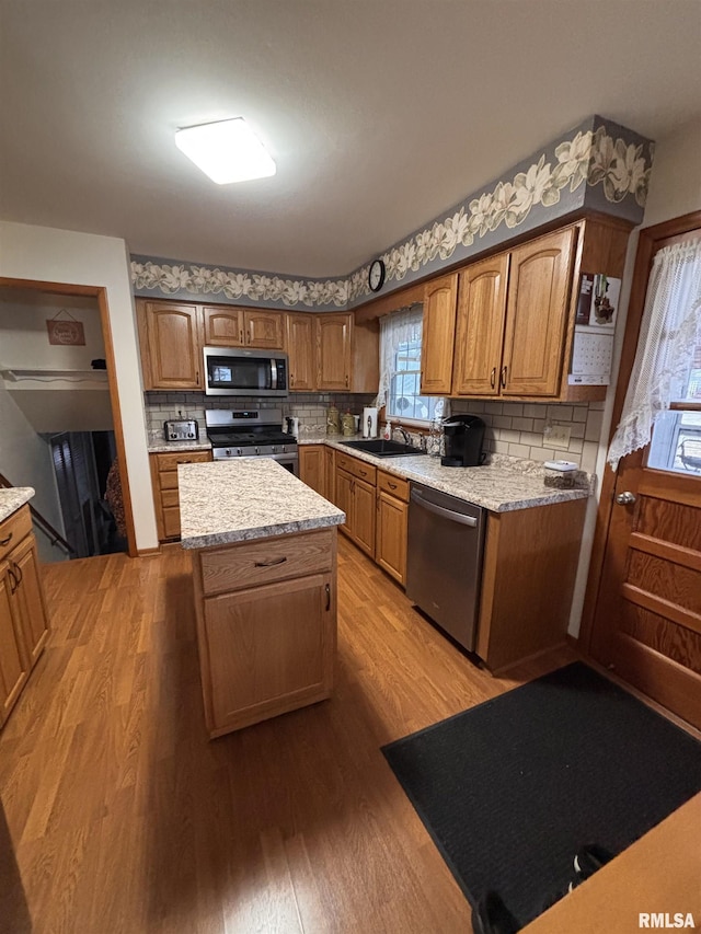 kitchen with stainless steel appliances, a sink, a kitchen island, wood finished floors, and brown cabinets