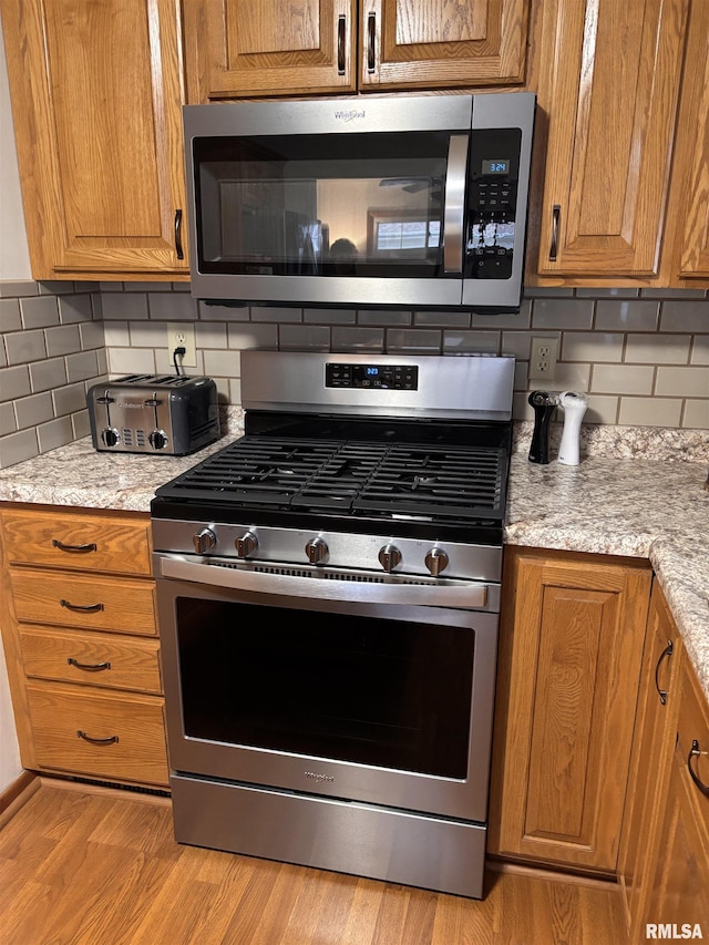 kitchen featuring appliances with stainless steel finishes, brown cabinetry, light wood-type flooring, and backsplash