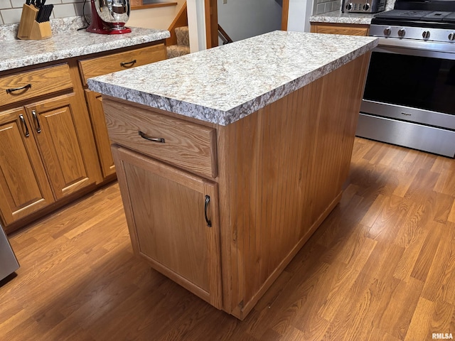 kitchen with light wood-style floors, a kitchen island, brown cabinetry, and stainless steel range with gas stovetop