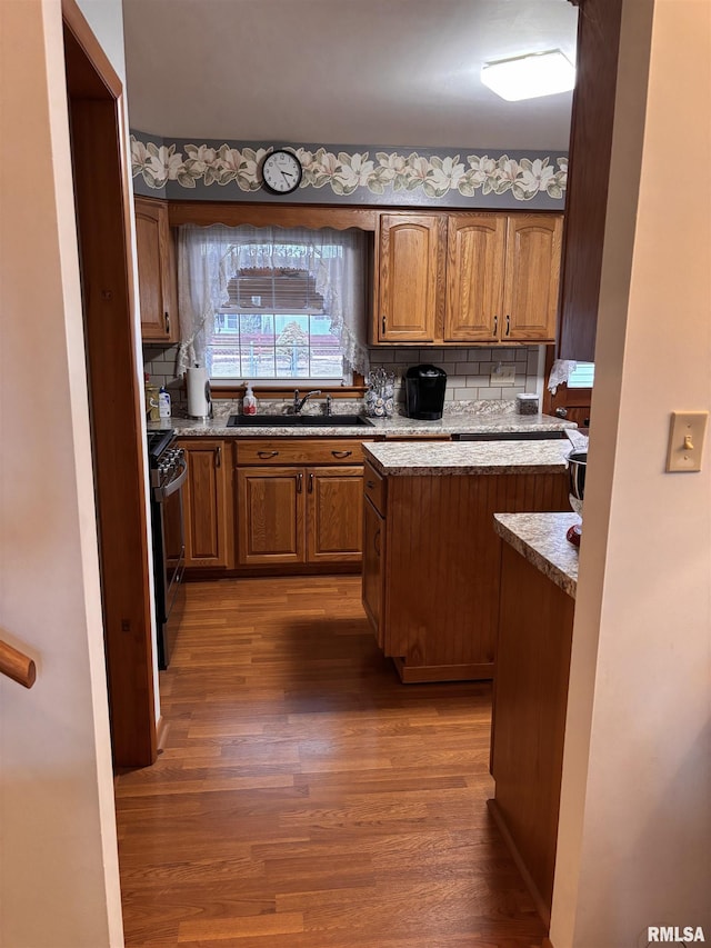 kitchen with tasteful backsplash, brown cabinetry, gas range, wood finished floors, and a sink