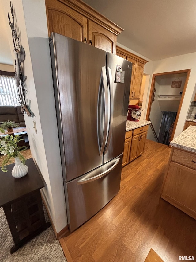 kitchen with light wood-style floors, light stone counters, brown cabinetry, and freestanding refrigerator