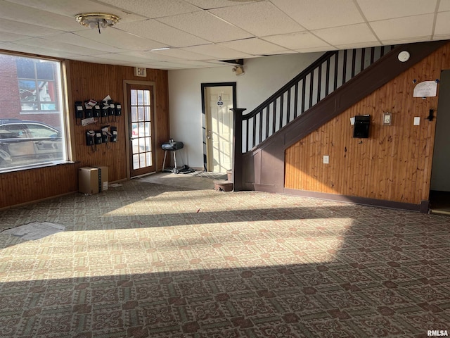 foyer entrance featuring stairs, wooden walls, baseboards, and a drop ceiling