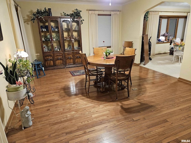 dining area with arched walkways, crown molding, and hardwood / wood-style flooring