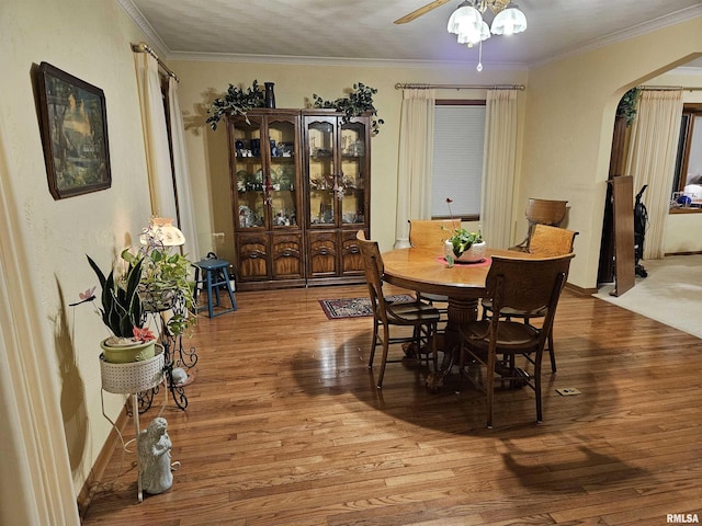 dining area featuring arched walkways, ornamental molding, and wood finished floors