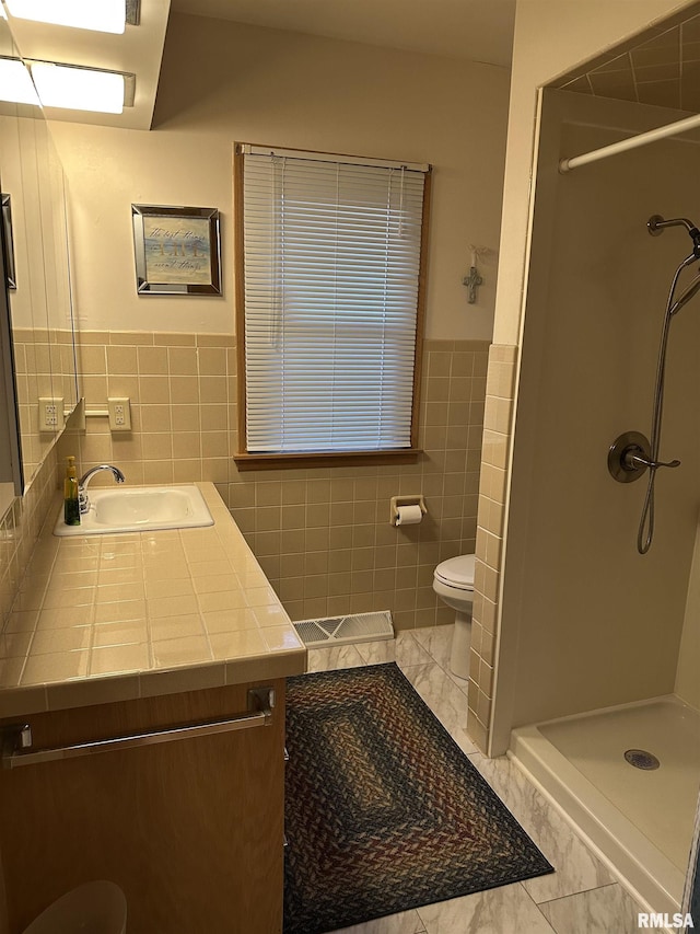 full bathroom featuring toilet, vanity, tile walls, marble finish floor, and a stall shower