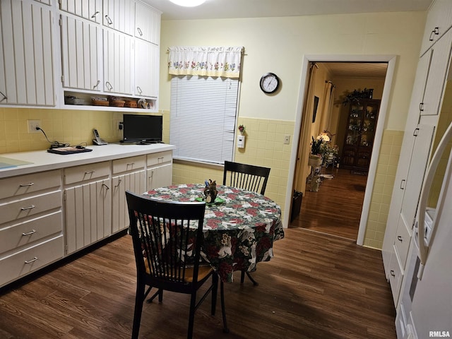 dining space with dark wood-type flooring, wainscoting, and tile walls