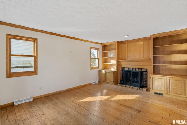 unfurnished living room with visible vents, a fireplace, a textured ceiling, and light wood finished floors