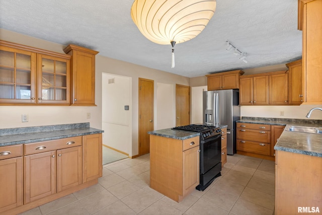 kitchen with stainless steel refrigerator with ice dispenser, dark countertops, black range with gas stovetop, a sink, and a textured ceiling