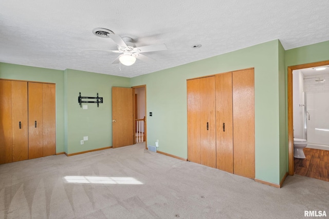 unfurnished bedroom with baseboards, visible vents, ensuite bathroom, a textured ceiling, and two closets