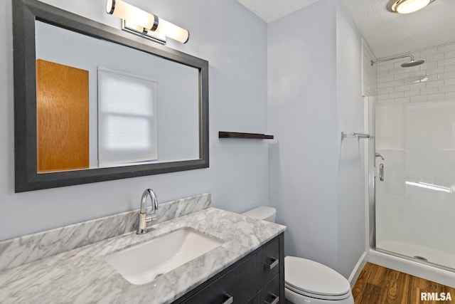 full bath with toilet, a stall shower, a textured ceiling, vanity, and wood finished floors