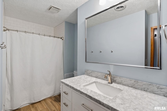 bathroom featuring a textured ceiling, vanity, wood finished floors, and visible vents